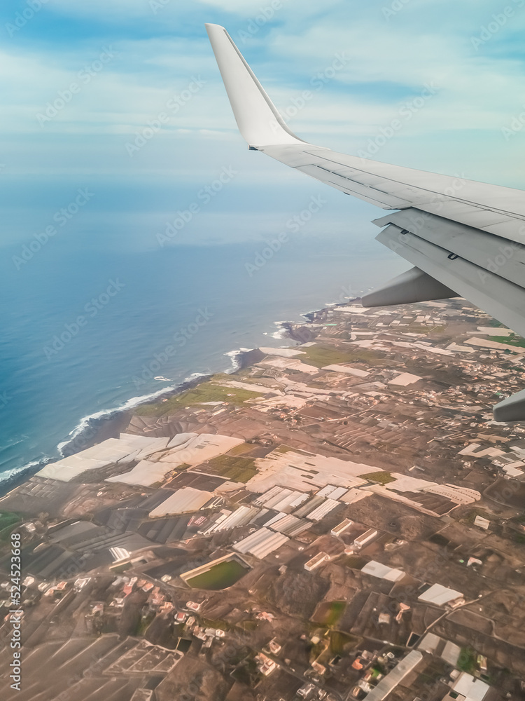 Airplane wing against the backdrop of the landscape of Tenerife and the Atlantic Ocean, vertical. View from the plane window on the coast of the Canary Islands