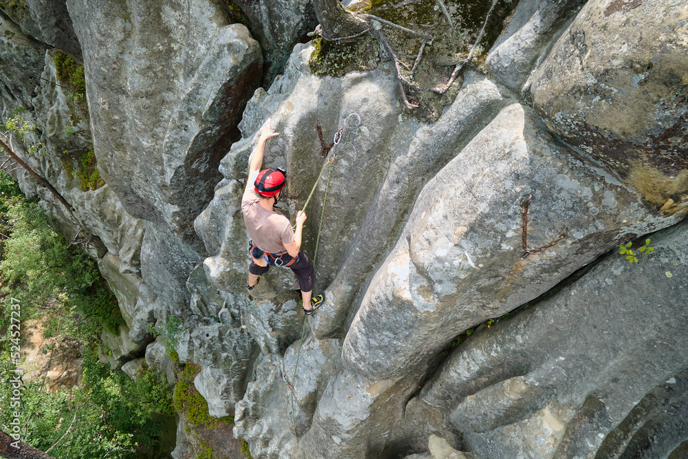 Determined climber clambering up steep wall of rocky mountain. Sportsman overcoming difficult route. Engaging in extreme sports and rock climbing hobby concept Determined climber clambering up steep wall of rocky mountain. Sportsman overcoming difficult route. Engaging in extreme sports and rock climbing hobby concept