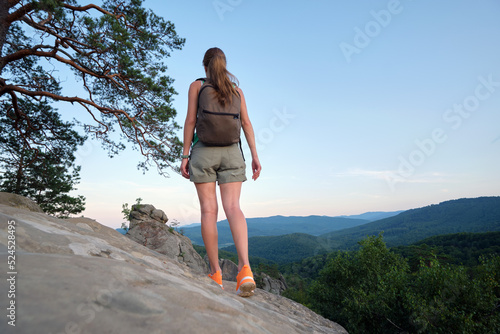 Sportive woman walking alone on hillside trail. Female hiker enjoying view of evening nature from rocky cliff on wilderness path. Active lifestyle concept