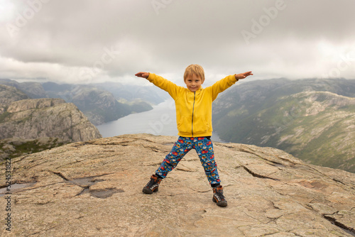 Family, enjoying the hike to Preikestolen, the Pulpit Rock in Lysebotn, Norway on a rainy day, toddler climbing with his pet dog the one of the most scenic fjords