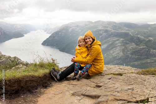 Family, enjoying the hike to Preikestolen, the Pulpit Rock in Lysebotn, Norway on a rainy day, toddler climbing with his pet dog the one of the most scenic fjords