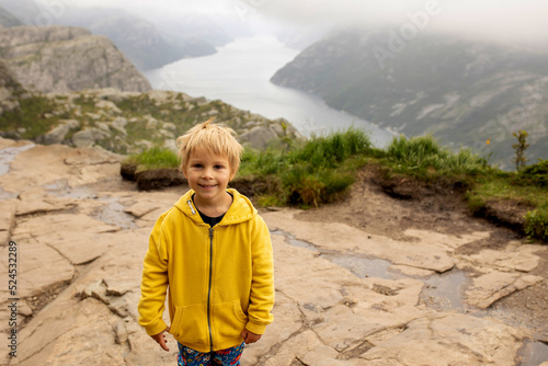 Family, enjoying the hike to Preikestolen, the Pulpit Rock in Lysebotn, Norway on a rainy day, toddler climbing with his pet dog the one of the most scenic fjords