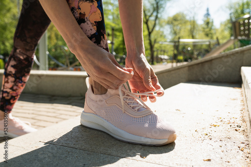 Young woman tying running shoes in the park outdoor, female runner ready for jogging on the road outside