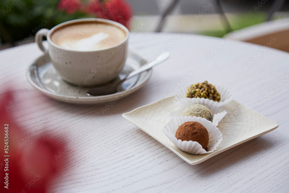 Natural vegan truffles without baking, flour and milk. Cup of cappuccino on wooden table outdoor in the cafe terrace. Coffee break. Natural vegan truffles without baking, flour and milk. Cup of cappuccino on wooden table outdoor in the cafe terrace. Coffee break.
