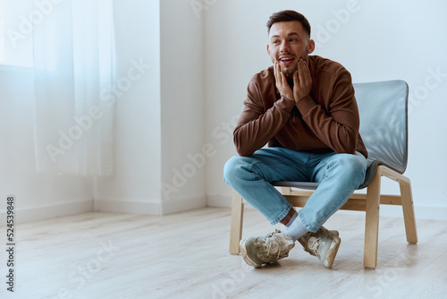 Fotografiet Excited shocked happy surprised young tanned man touch cheeks looks aside dreaming about holiday plans cool idea for startup have insight sitting in chair at home