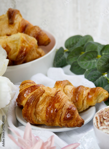 Fresh homemade croissants on a white plate against the background of a bowl of buns