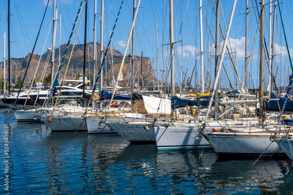 boats and yachts on pier in marine city port with masts and bulidings and blue sky on background
