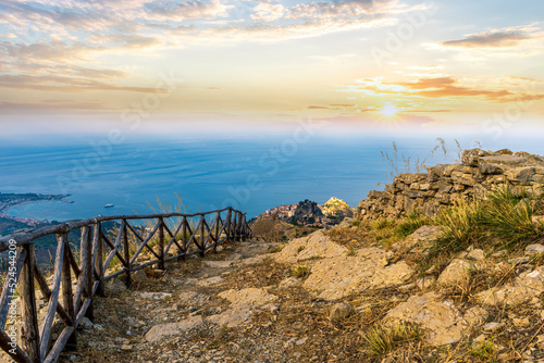 mountain landscape with a hiking trail leading to a mountain town and beautiful blue seashore far away