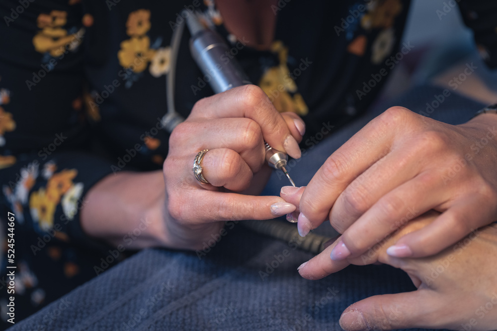 Obraz premium nail grinding and polishing, i.e. professional hardware woman's hand manicure with an electric drill at the client's house. machine removal of protruding cuticles. closeup photo.