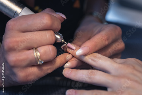 professional manicure with an electric drill, removal of protruding cuticles by nails, smoothing and polishing nails during a home visit. closeup shot.