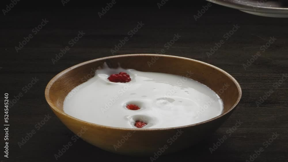 Fresh raspberries fall into a wooden plate with cream. Medium plan Fresh raspberries fall into a wooden plate with cream. Medium plan