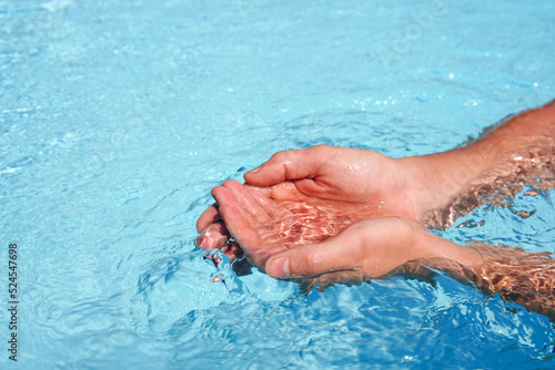 The hands cupped together submerged in clean clear blue water in swimming pool