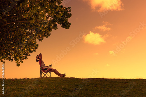 Sit back relax take a break! Woman sitting in a field at sunset having feelings of freedom, and happiness in nature 