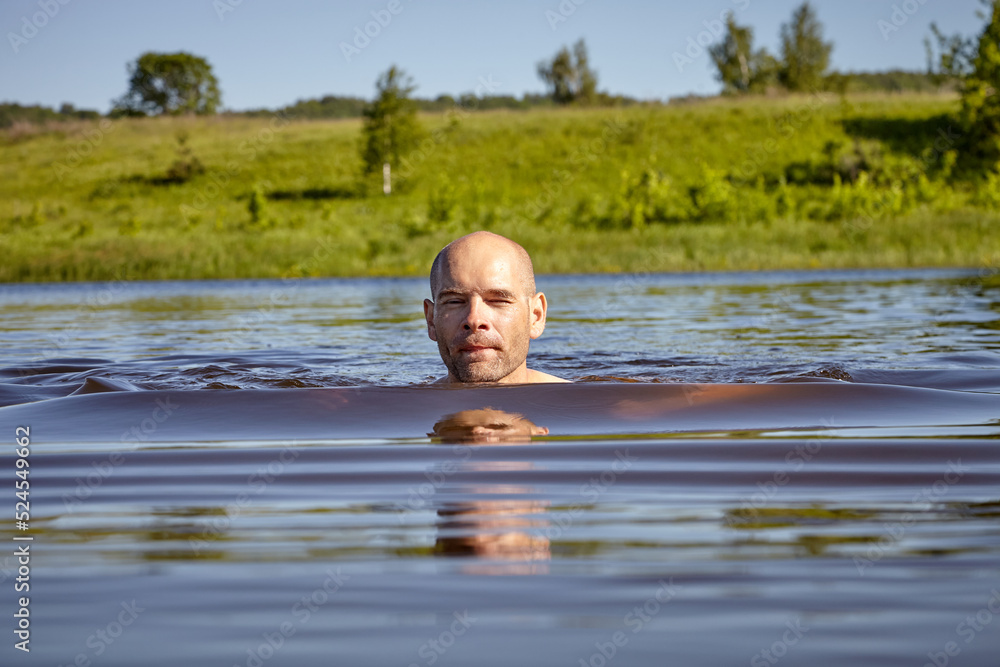 Fototapeta premium Bald guy swims on the river in summer