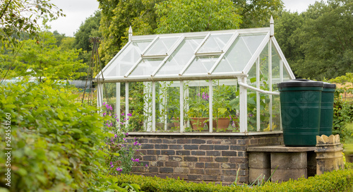 Two green water butts outside a greenhouse being used for water storage, water collection system in place, eviromental concept