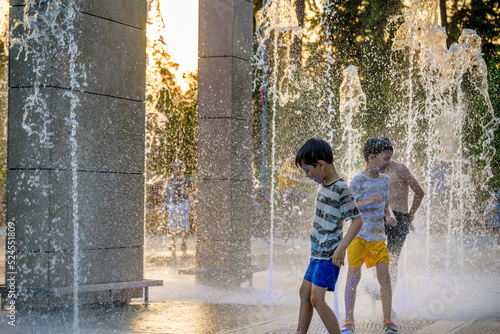 Boys jumping in water fountains. Children playing with a city fountain on hot summer day. Happy friends having fun in fountain. Summer weather. Friendship, lifestyle and vacation