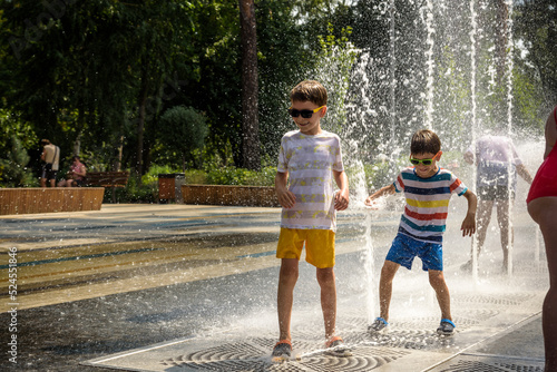 Boy having fun in water fountains. Child playing with a city fountain on hot summer day. Happy kids having fun in fountain. Summer weather. Active leisure, lifestyle and vacation