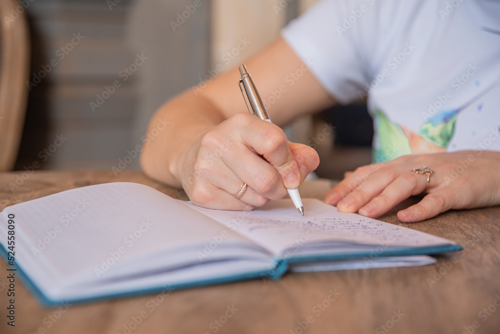 Close up view of woman sit at table hold pen take notes to paper notebook working studying Close up view of woman sit at table hold pen take notes to paper notebook working studying