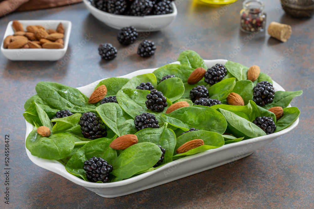 Spinach Salad with blackberries, almonds and lemon oil dressing on a white plate with ingredients on background. Spinach Salad with blackberries, almonds and lemon oil dressing on a white plate with ingredients on background.