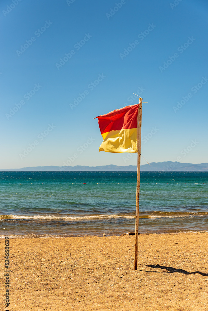 lifeguard icon on the beach , lifeguard flag waving in the wind to inform people , yellow red flag and the sea in the background