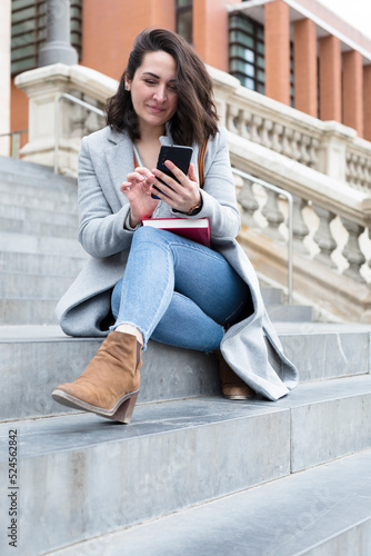 Elegant young caucasian woman using mobile phone. She is sitting on some steps outdoors. © Alfredo López