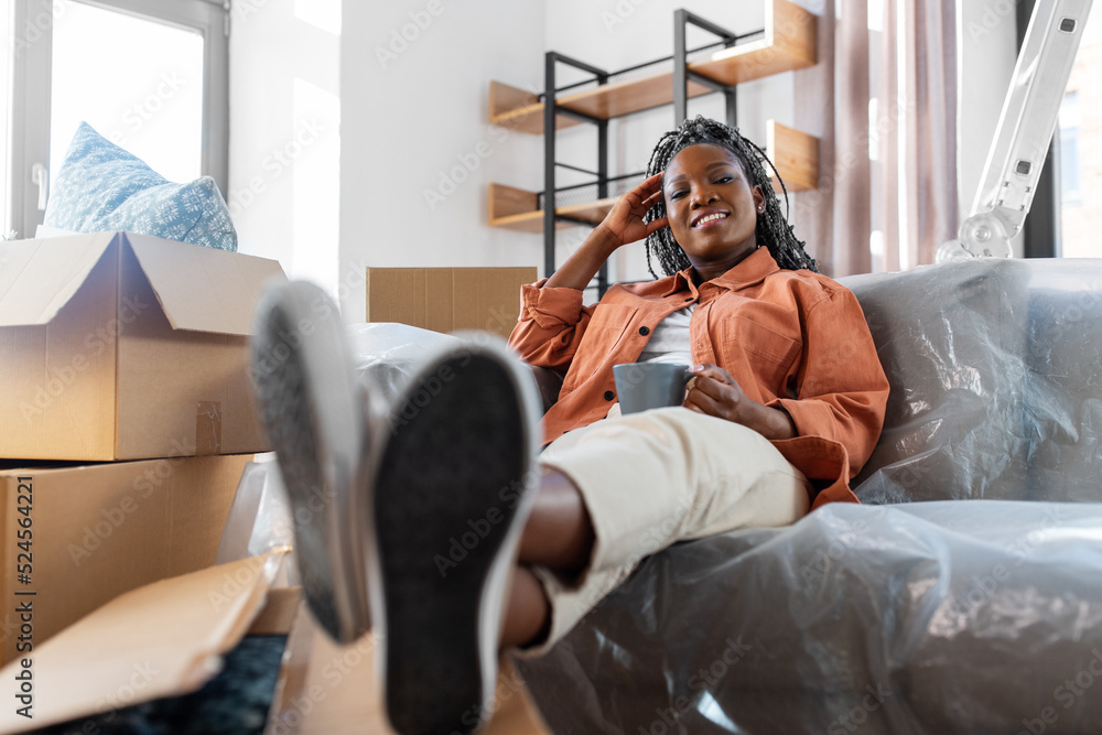Obraz premium moving, people and real estate concept - happy smiling woman with boxes sitting on sofa with cup of coffee at new home