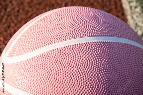 Pink basketball ball on the ground. Close-up ball on the red court. Basketball on the street or indoor court. Sports gear without people. Minimalism. Template, sport background 