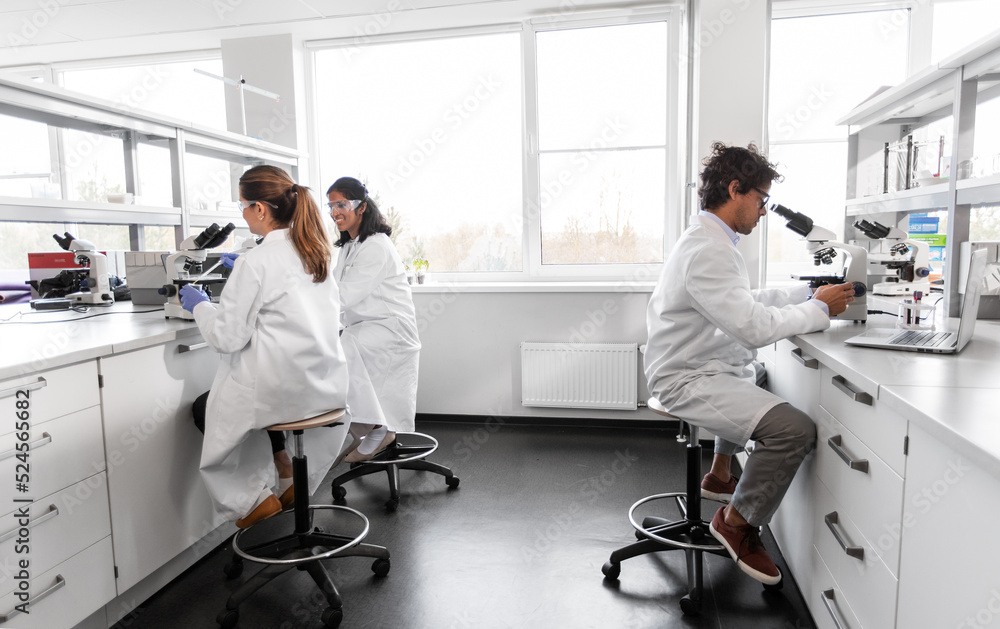 Fototapeta premium science research, work and people concept - international group of scientists with microscopes working in laboratory