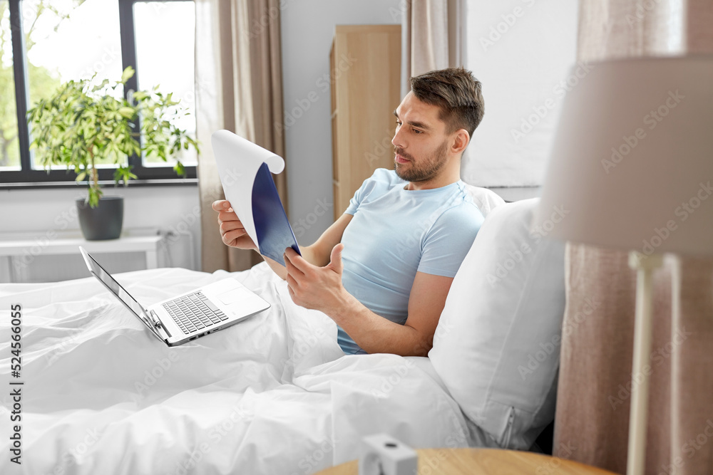 people, technology and remote job concept - man with laptop computer and clipboard working in bed at home bedroom people, technology and remote job concept - man with laptop computer and clipboard working in bed at home bedroom