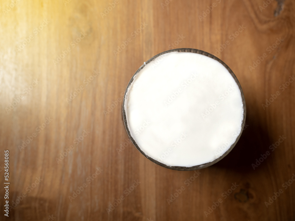 White milk in coffee cup on wooden table with yellow light on left side by top view White milk in coffee cup on wooden table with yellow light on left side by top view