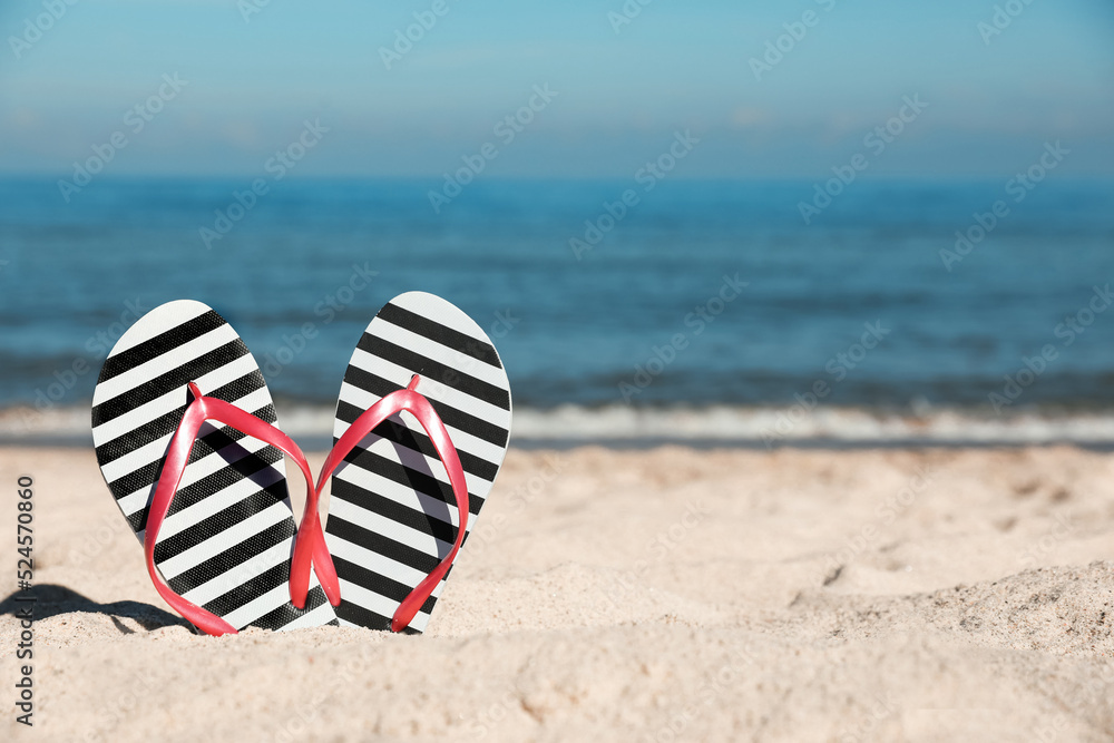 Naklejka premium Striped flip flops in sand on beach near sea. Space for text