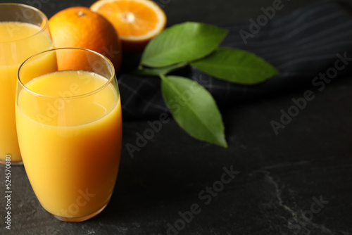 Glasses of orange juice and fresh fruits on black table. Space for text