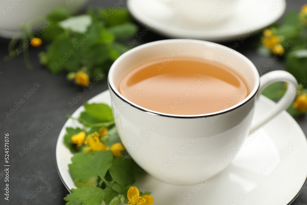 Cup of aromatic celandine tea and flowers on black table, closeup Cup of aromatic celandine tea and flowers on black table, closeup
