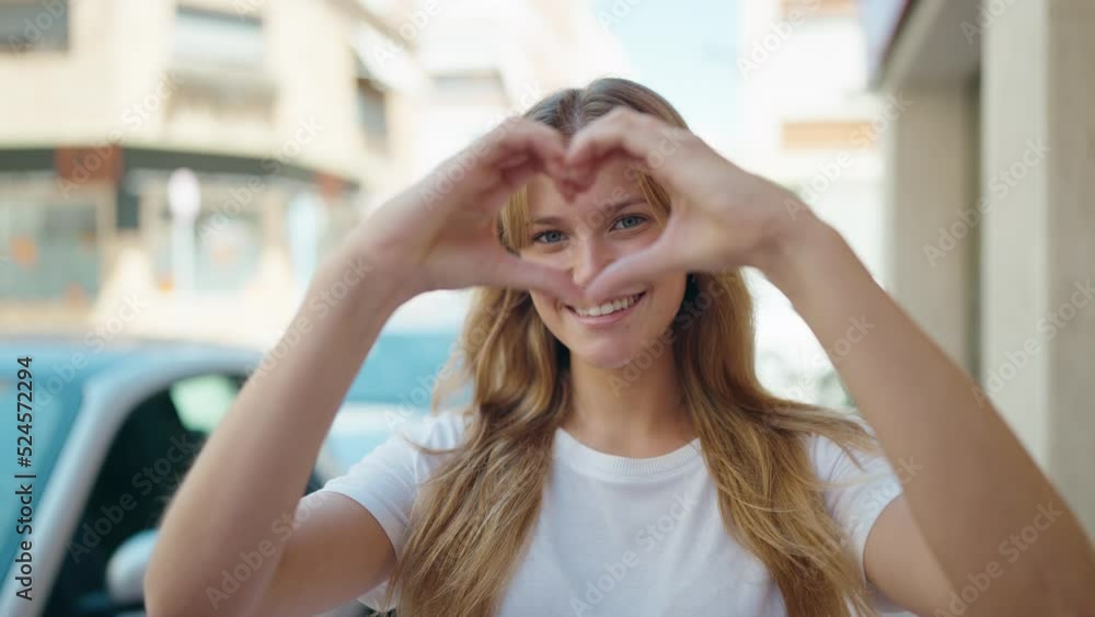 Young blonde girl smiling confident doing heart gesture with hands at street Young blonde girl smiling confident doing heart gesture with hands at street