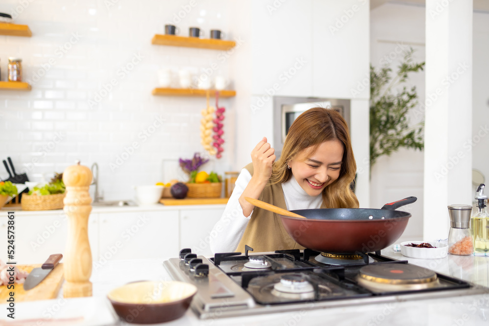 Young beautiful Asian woman enjoy cooking healthy food and pasta in cooking pan on stove in the kitchen at home. Happy female having dinner meeting party celebration with friends on holiday vacation.