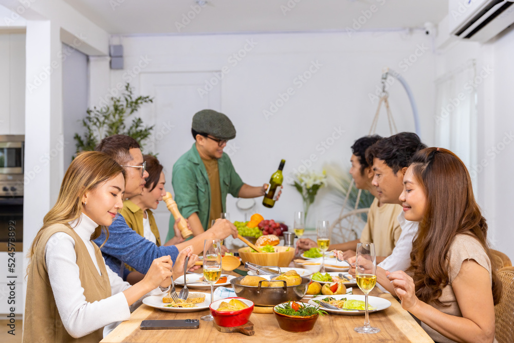 Group of Asian man and woman friends having dinner with drinking wine and talking together on dining table at home. Happy people friendship enjoy reunion meeting celebration party on holiday vacation