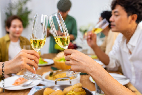 Group of Cheerful Asian man and woman friends toasting wine glasses while having dinner together at home. Happy male and female reunion meeting event celebrating party on holiday vacation