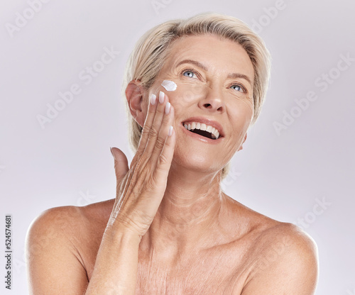 Woman with sunscreen on face for beauty skincare, showing cosmetics with smile and care for skin wellness standing on grey studio background. Content elderly model doing self care with cream