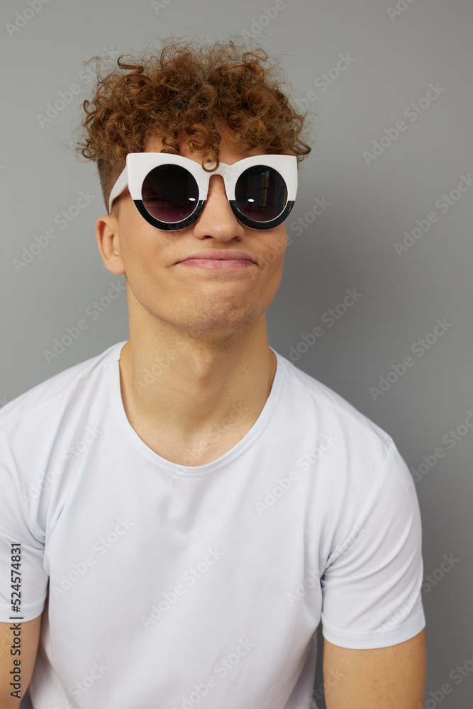 a crazy, funny man with curly hair stands on a gray background making a funny grimace funny wearing glasses on the contrary. Close horizontal portrait a crazy, funny man with curly hair stands on a gray background making a funny grimace funny wearing glasses on the contrary. Close horizontal portrait