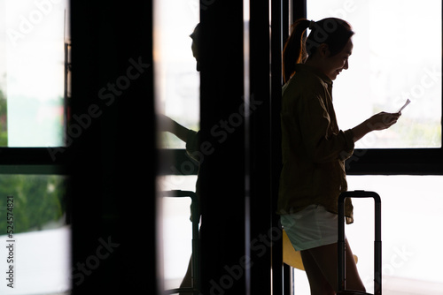 Silhouette of Asian woman passenger checking flight boarding time on boarding pass and walking to boarding gate in airport terminal. Woman tourist go travel destination by airplane on holiday vacation