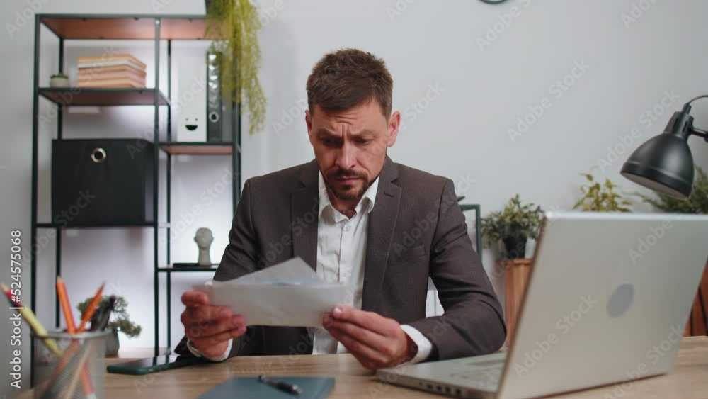 Stressed businessman in suit working looking at unpaid bank debt bills, doing paperwork, planning budget, calculate finances mortgage payments at office. Displeased freelancer man throws paper bills Stressed businessman in suit working looking at unpaid bank debt bills, doing paperwork, planning budget, calculate finances mortgage payments at office. Displeased freelancer man throws paper bills