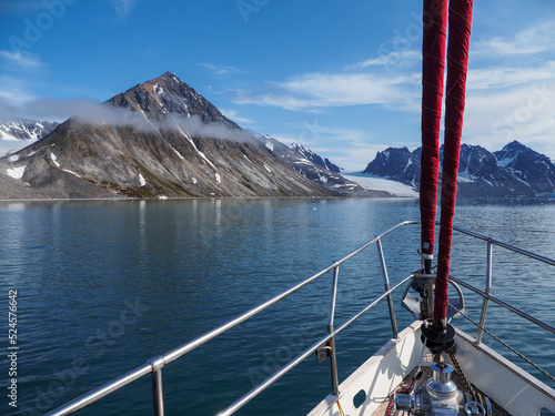 A sailboat navigating calm Arctic waters, surrounded by majestic mountains under a clear blue sky. Svalbard Norway photo