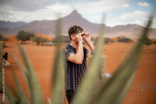 male traveler looking through binoculars in desert safari of namibia africa