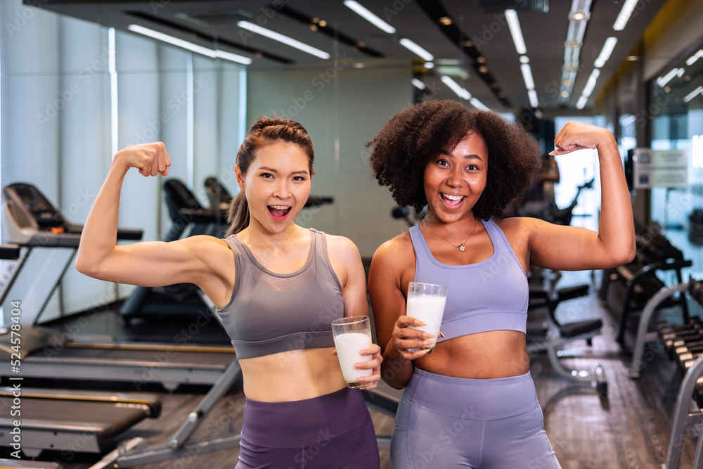 Asian and African American woman finishing workout and drinking protein milk shake vitamins after training. Bodybuilding. Healthy Friend lifestyle. Asian and African American woman finishing workout and drinking protein milk shake vitamins after training. Bodybuilding. Healthy Friend lifestyle.