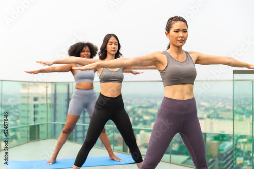 Young Asian woman and African American exercise yoga on the rooftop.Group of happy fit friends exercising outdoor in city.