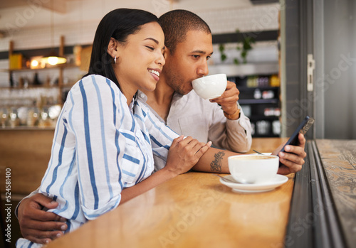 Couple using social media on a phone and drinking tea in a coffee shop together. Happy man and woman with 5g mobile smartphone texting and searching on an online app and enjoy a date at a cafe