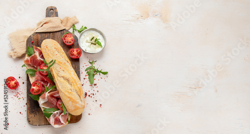 Fototapeta Naklejka Na Ścianę i Meble -  Fresh crispy baguette deli sandwich with prosciutto, tomatoes and arugula.