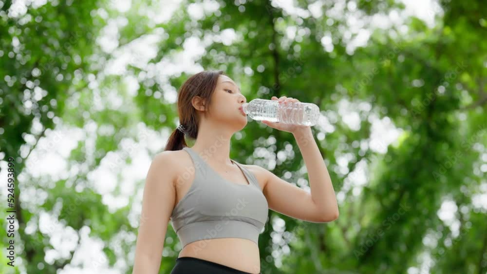 Young asian woman drinking water from a bottle while taking a break during her workout. Happy adolescence female working out in the park and taking rest a break to drink water Young asian woman drinking water from a bottle while taking a break during her workout. Happy adolescence female working out in the park and taking rest a break to drink water