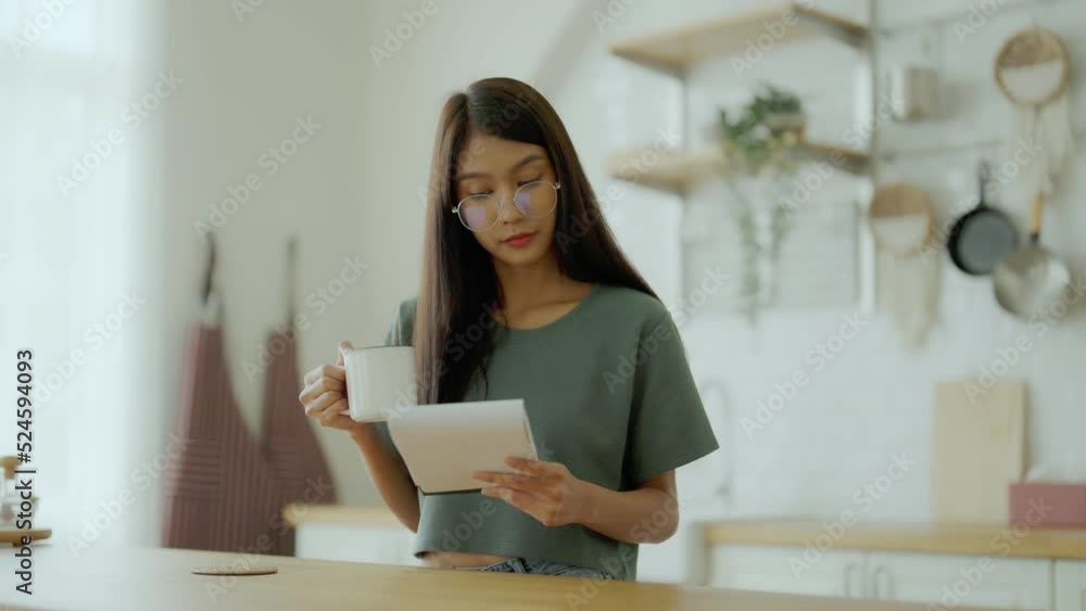Happy young asian woman wearing glasses in kitchen at home. Female concentrate reading note cooking Happy young asian woman wearing glasses in kitchen at home. Female concentrate reading note cooking
