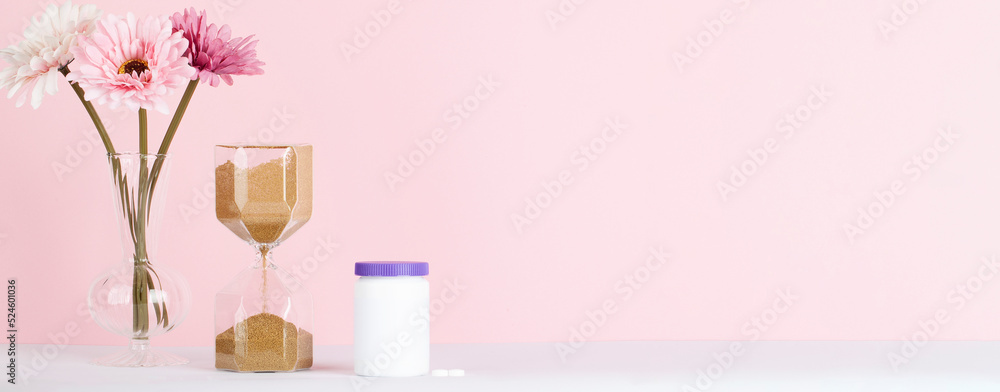 women health concept. medicine, health care style. copy space. white plastic bottle with pills, flowers and hourglass on beige background. banner